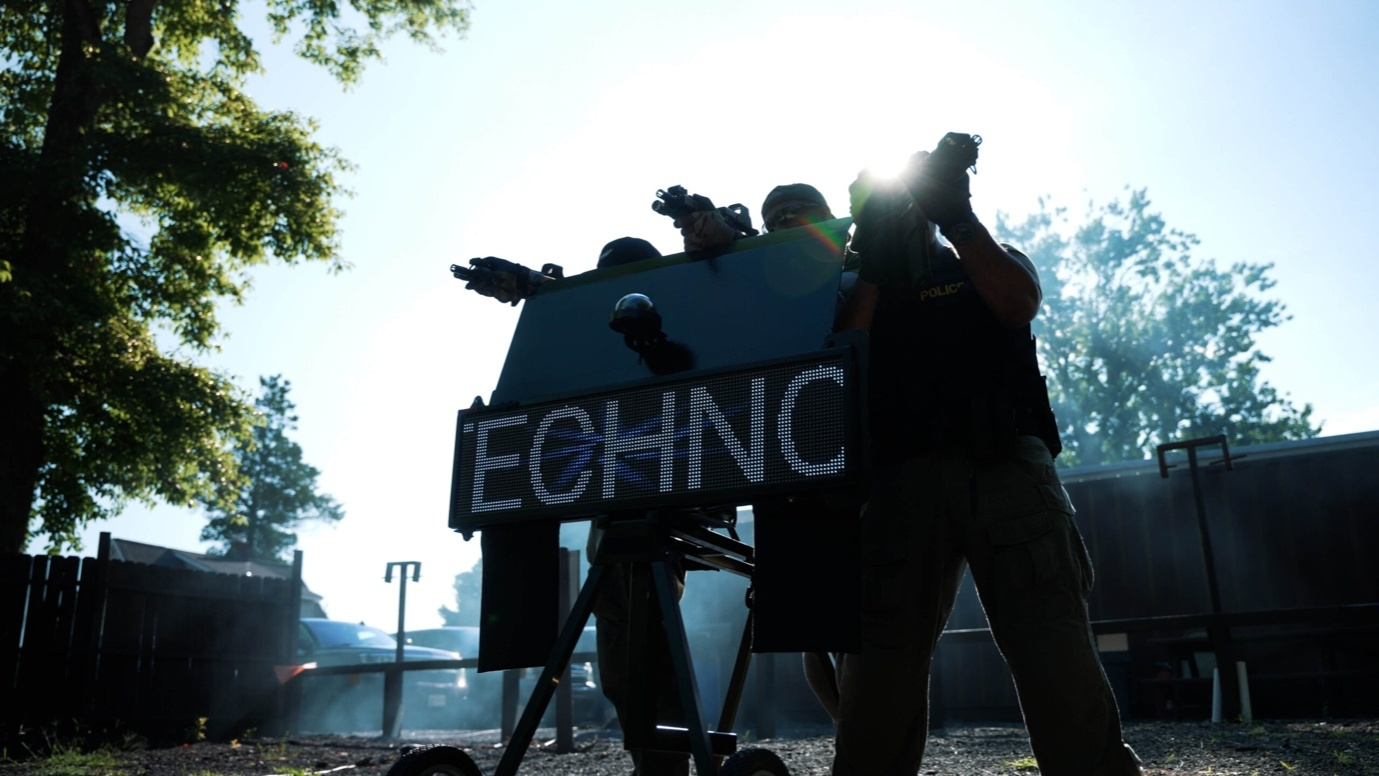 A Tactical Team Aiming Their Weapons in Different Directions While Standing Behind a Moving Message Display